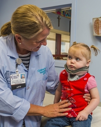 female neurosurgeon with blonde hair supports a female toddler in a red dress